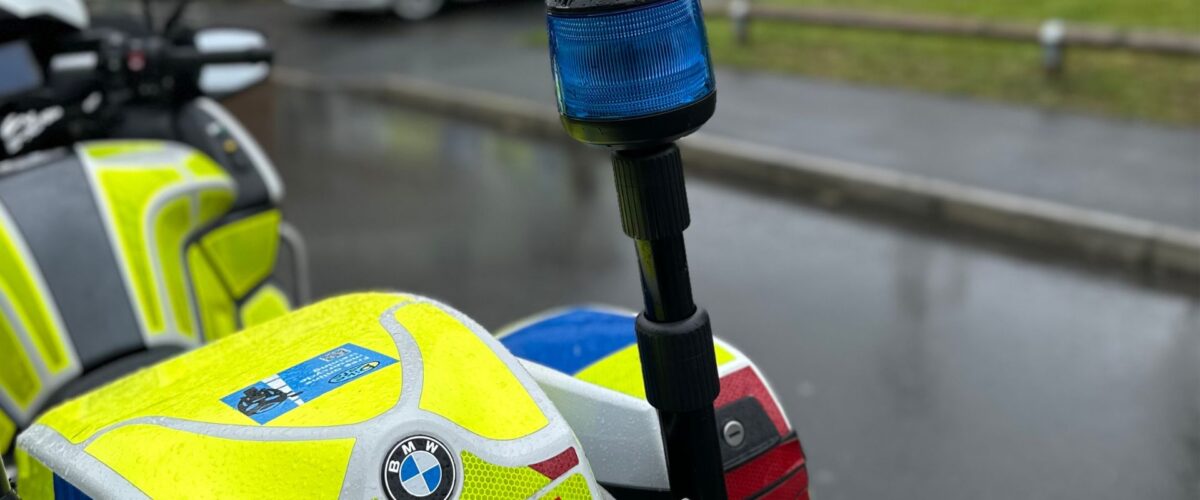 Picture of West Mercia Police bike on the side of a road on a rainy day. The police bike is sat in a housing estate.